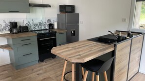 A modern kitchen with a central island, bar stools, a built-in oven, and a microwave. - Charming fully-equipped house (La Houssière)