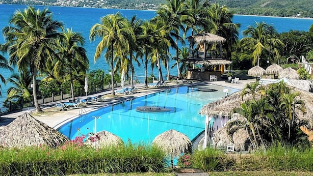 A pool with lounge chairs and palm trees, surrounded by thatched-roof structures. - T2 Ti Madinina sea view with pool Le Diamant (Le Diamant)