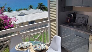 A balcony with a table and chairs, a view of the ocean, and a kitchen area with cabinets and a sink. - T2 Ti Madinina sea view with pool Le Diamant (Le Diamant)