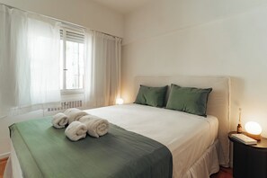 A neatly made bed with green bedding, a bedside lamp, and a window with curtains. - Hestia at Talcahuano 1100 (Buenos Aires)