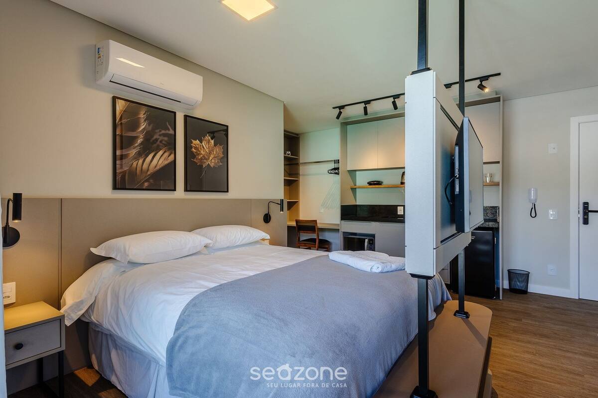 Quarto de hotel moderno com uma cama grande, televisão de tela plana e uma cozinha compacta.