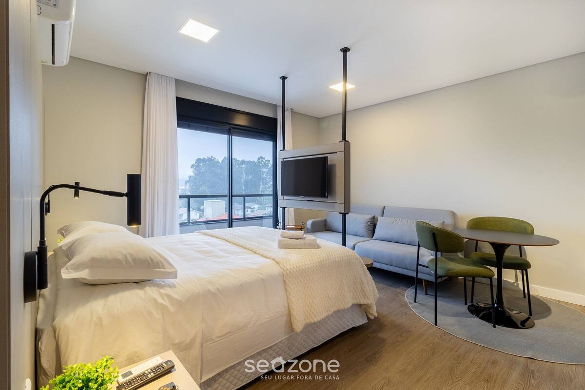 Quarto de hotel moderno com uma cama grande, um sofá, uma mesa pequena e uma televisão.