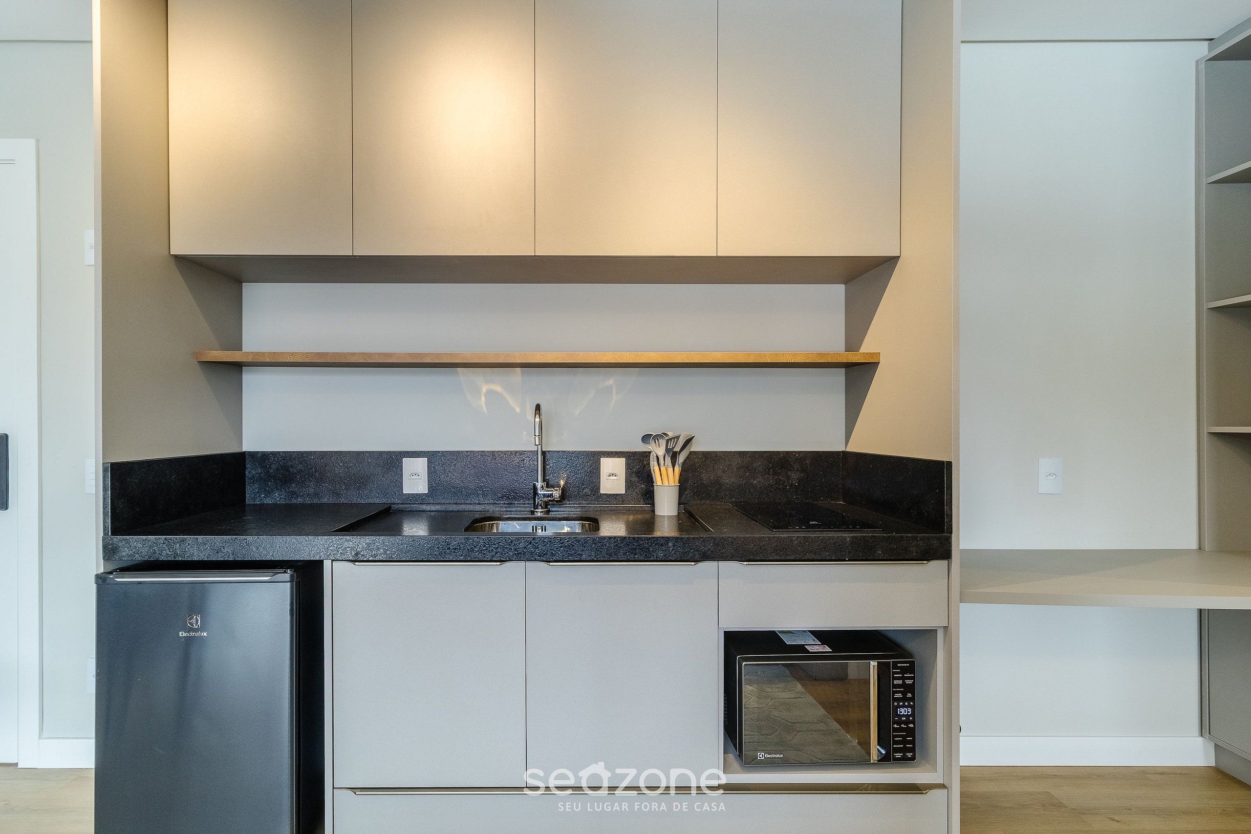 Cozinha moderna com eletrodomésticos embutidos, incluindo lava-louças, micro-ondas e uma pia com torneira.