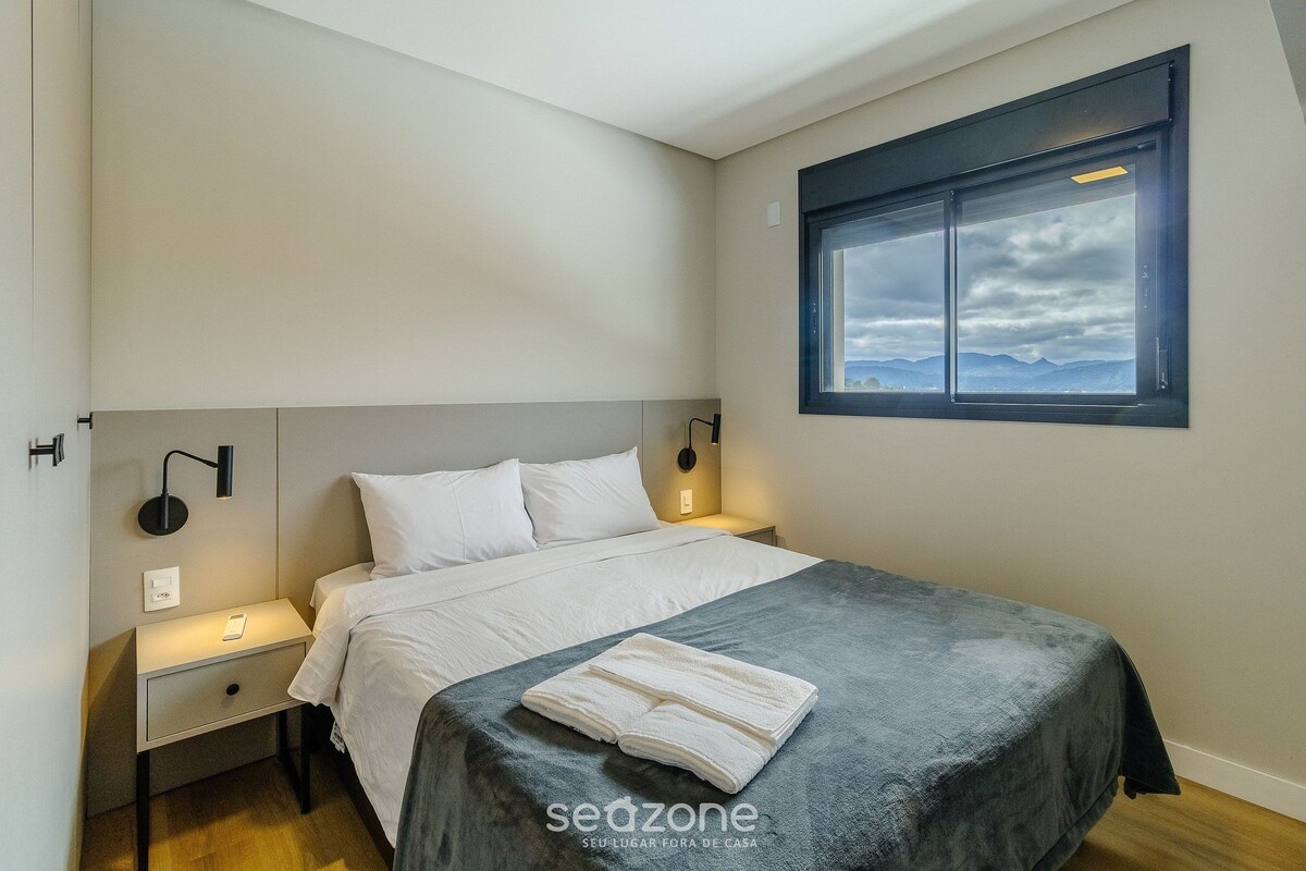 A bedroom with a bed, bedside lamps, a nightstand, a window with a view, and a towel on the bed.