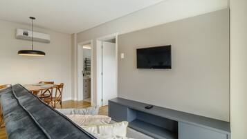 Una sala moderna con un sofá gris, una mesa de comedor con sillas, un televisor de pantalla plana montado en la pared y un banco empotrado debajo del televisor.