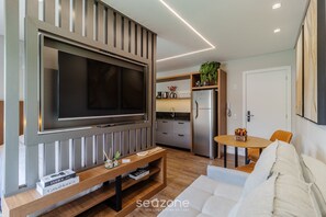 Ett modernt vardagsrum med en stor platt-TV som är monterad på väggen, ett träbord med böcker, en soffa och en matplats med ett litet bord och stolar.