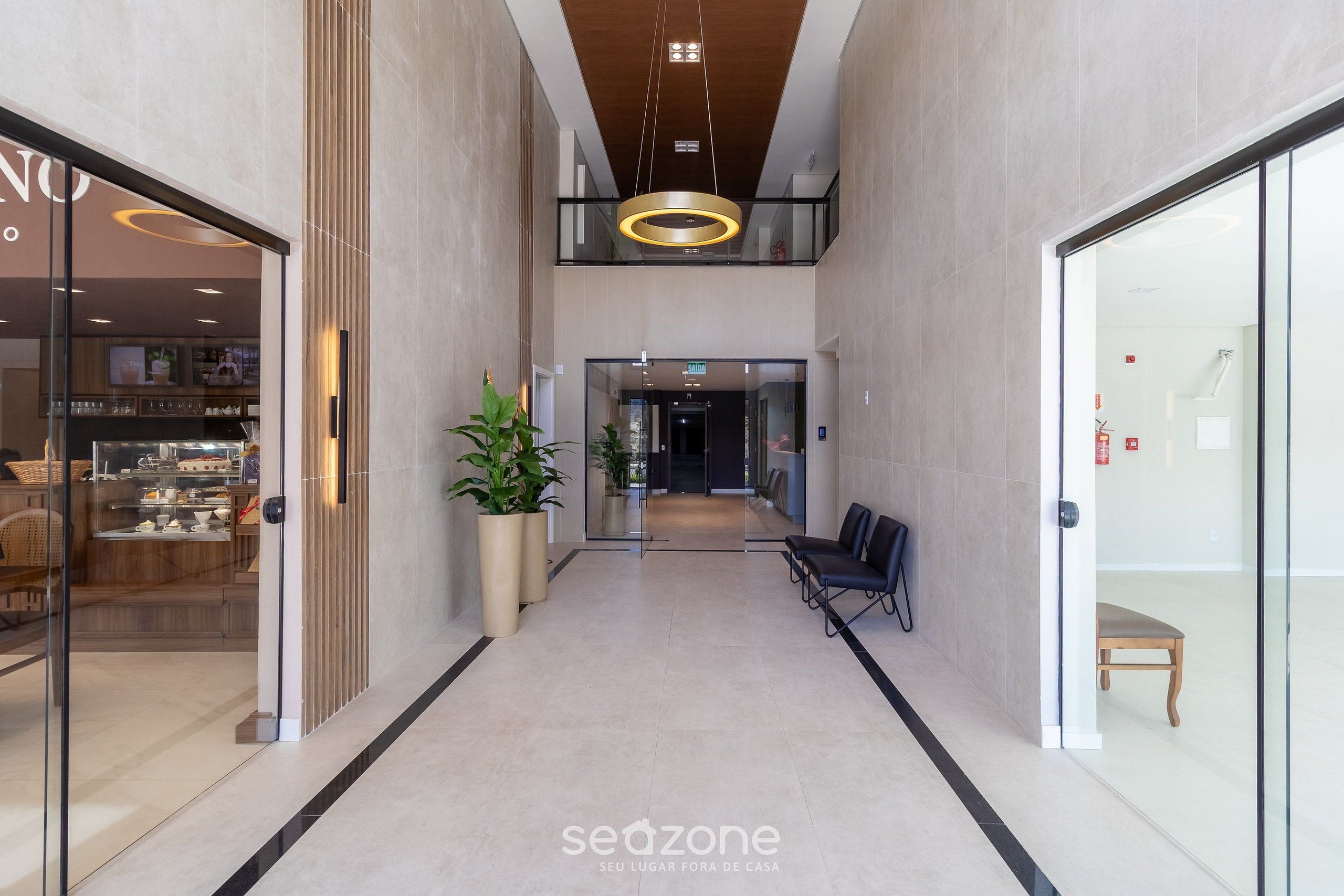 Un interior moderno con un pasillo central, zona de estar y puertas de cristal que dan a un restaurante.