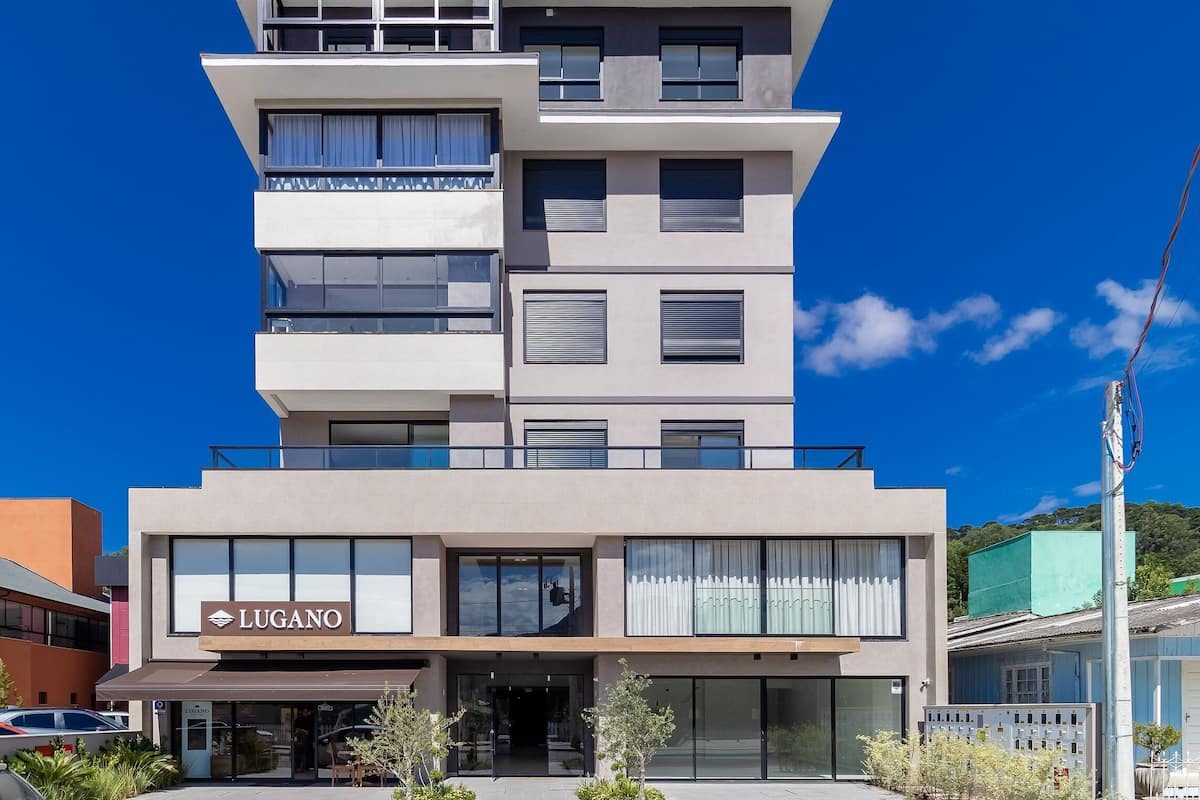 Um hotel de vários andares com design moderno, apresentando uma placa chamativa 'LUGANO' na entrada.