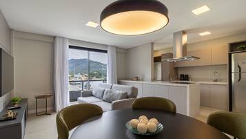 A modern kitchen with a built-in island, a dining area with a round table, and a sofa by a large window overlooking a cityscape.