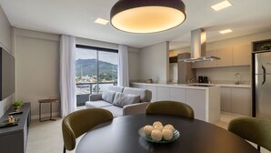 Una cocina moderna con una isla integrada, un comedor con mesa redonda y un sofá junto a un ventanal con vistas a la ciudad.