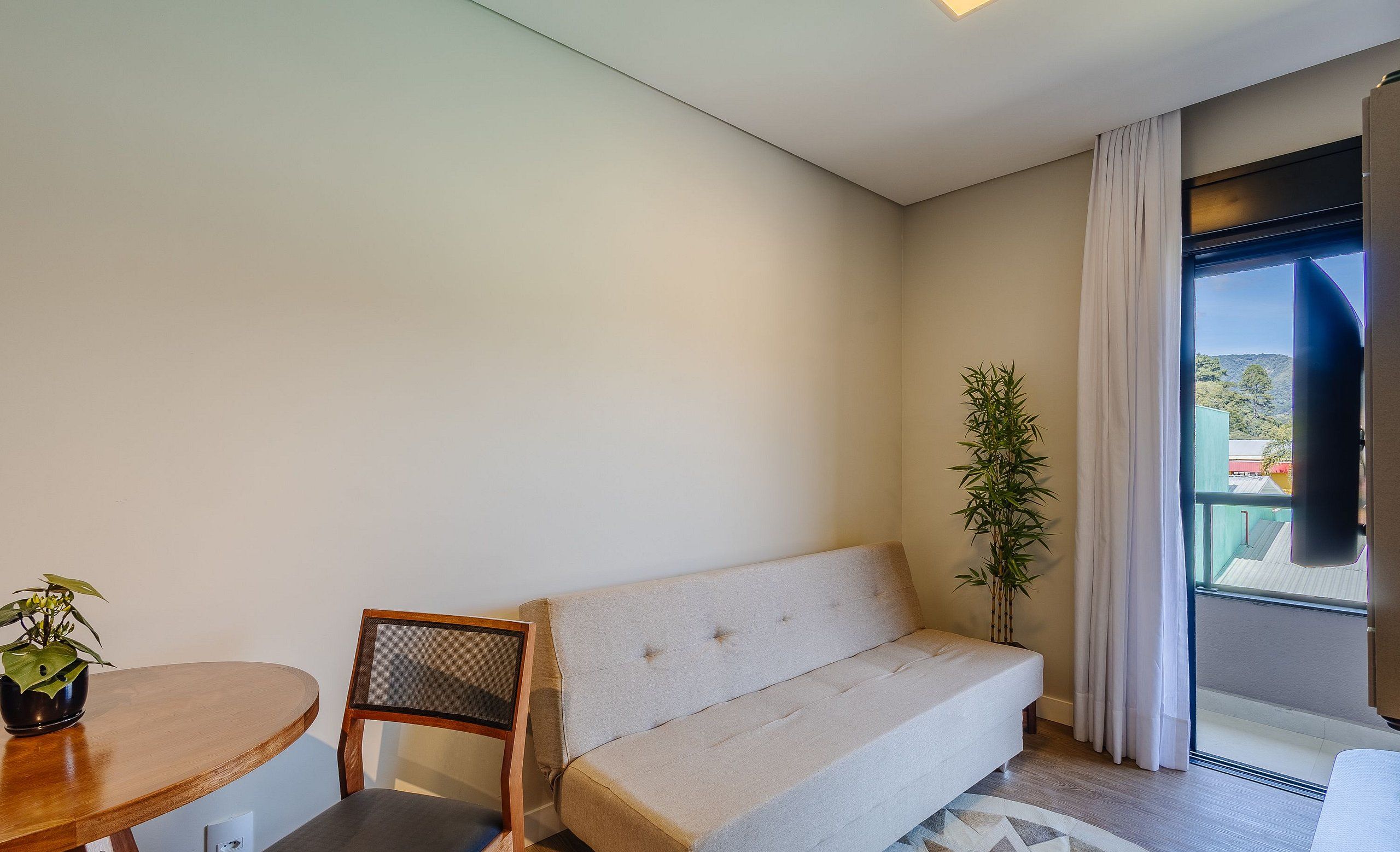 Una sala de estar moderna con un sofá, una mesa de comedor con sillas, una planta en maceta y vistas a través de un gran ventanal.