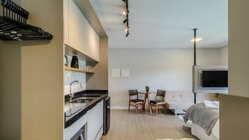 A modern kitchen with a dishwasher, a dining area with a table and chairs, and a bedroom with a bed and a TV.
