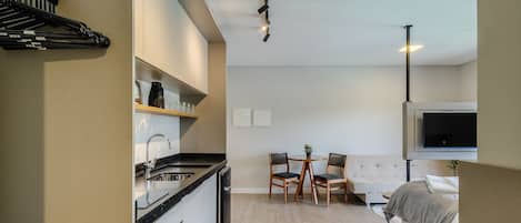 A modern kitchen with a dishwasher, a dining area with a table and chairs, and a bedroom with a bed and a TV.
