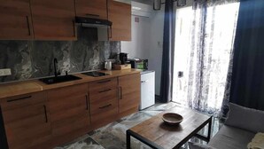 Una cocina moderna con armarios de madera, un lavamanos negro y un microondas. Hay una mesa de comedor con un bol y un sofá en la sala de estar.