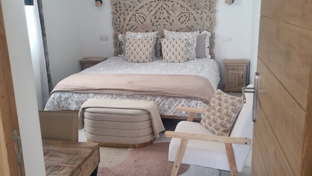 Quarto com cama grande, cabeceira de madeira, mesa de cabeceira, cadeira e uma pequena mesa.