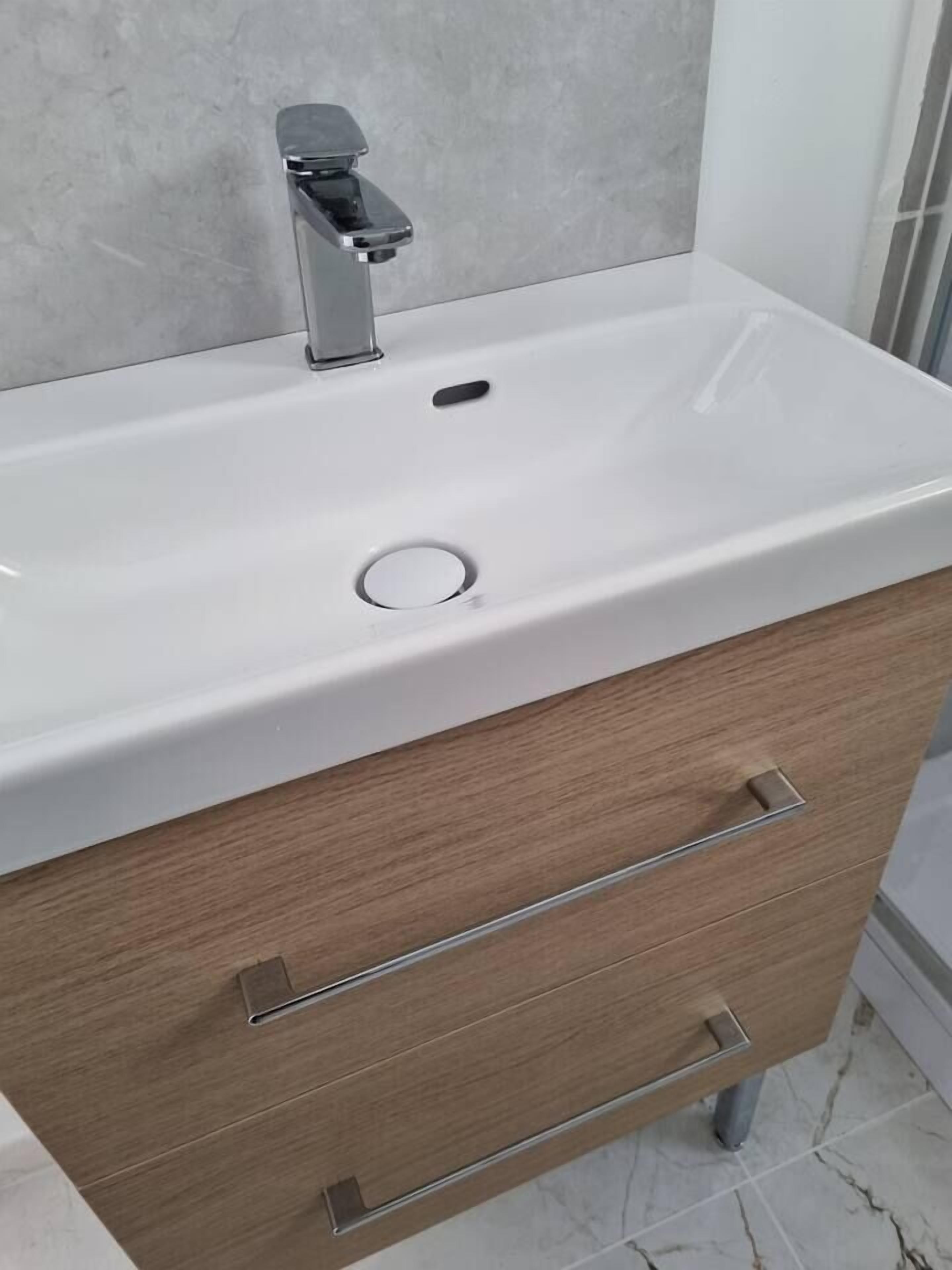 A bathroom vanity with a white sink, a single drawer, and a mirror above the sink.
