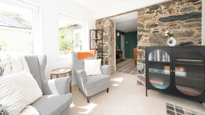 A living room with a houndstooth patterned armchair, a round side table, and a black cabinet with glass doors. - The Garden Cottage With Hot Tub, Pet Friendly! (Portsoy)