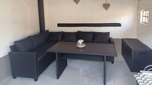 Un coin salon avec un canapé en osier foncé, une petite table agrémentée d’un objet décoratif et un haut-parleur noir.