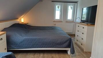A bedroom with a bed, a dresser, a television, and two windows with heart-shaped decorations.