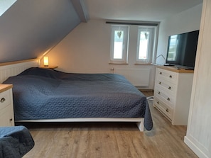 Une chambre à coucher comprenant un lit, une commode, un téléviseur et deux fenêtres décorées de motifs en forme de cœur.