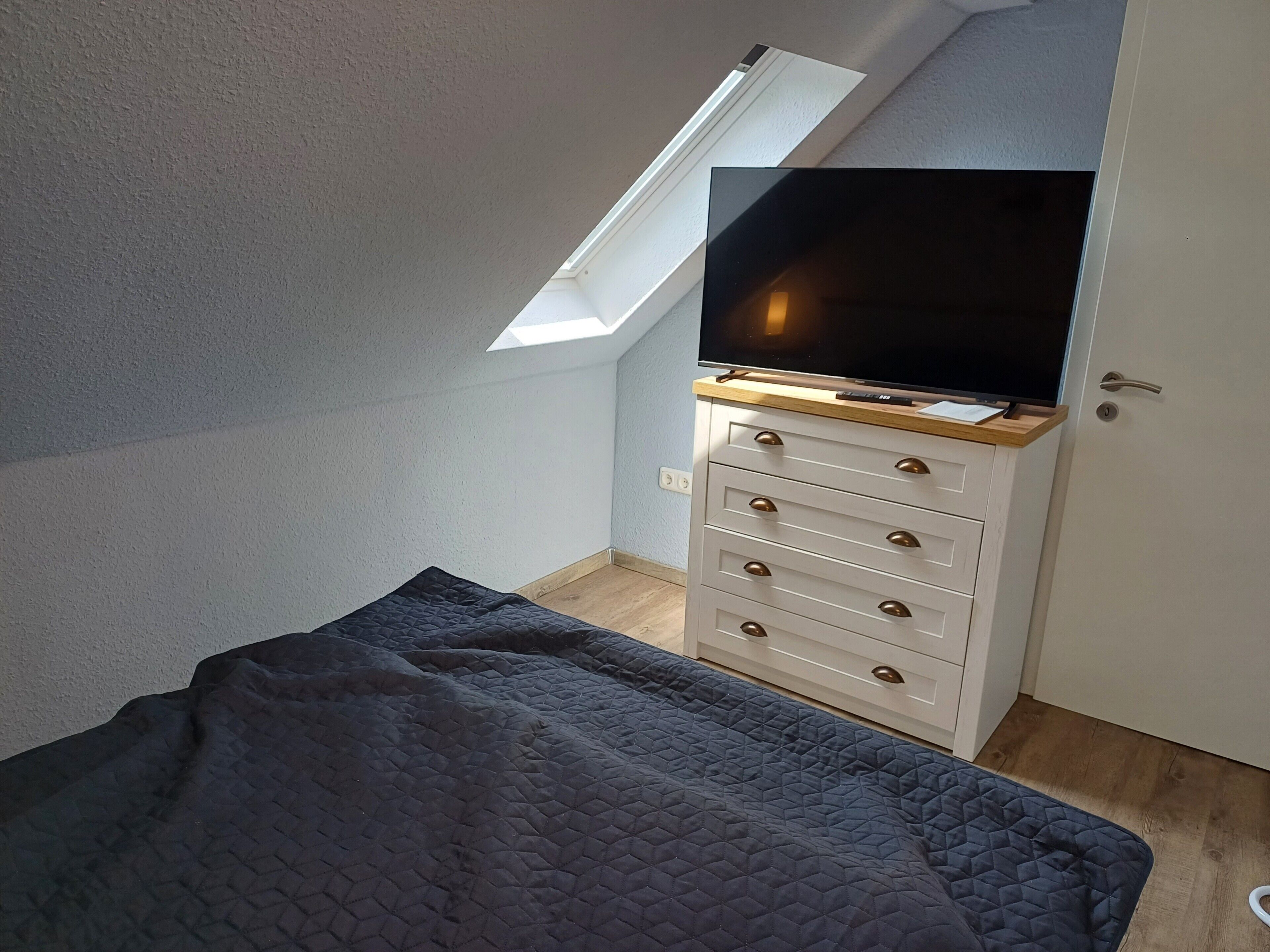 Ein Zimmer mit einem Bett, einem Fernseher auf einer Holzkommode, einem Oberlicht und einer Tür.