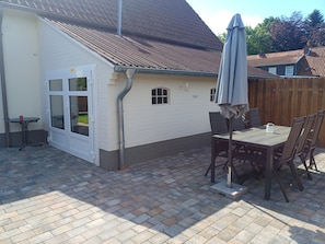 Une terrasse avec une table et des chaises, une porte blanche et un toit marron.