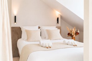 A neatly made bed with white linens and pillows, a vase with dried flowers, and two wall-mounted lights. - 1537 Bourg Tibourg (Paris)
