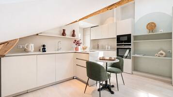 A modern kitchen with white cabinetry, a dining area with two green chairs, and a built-in oven.