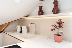 A modern kitchen with a marble countertop, a built-in sink, a kettle, and a potted plant.