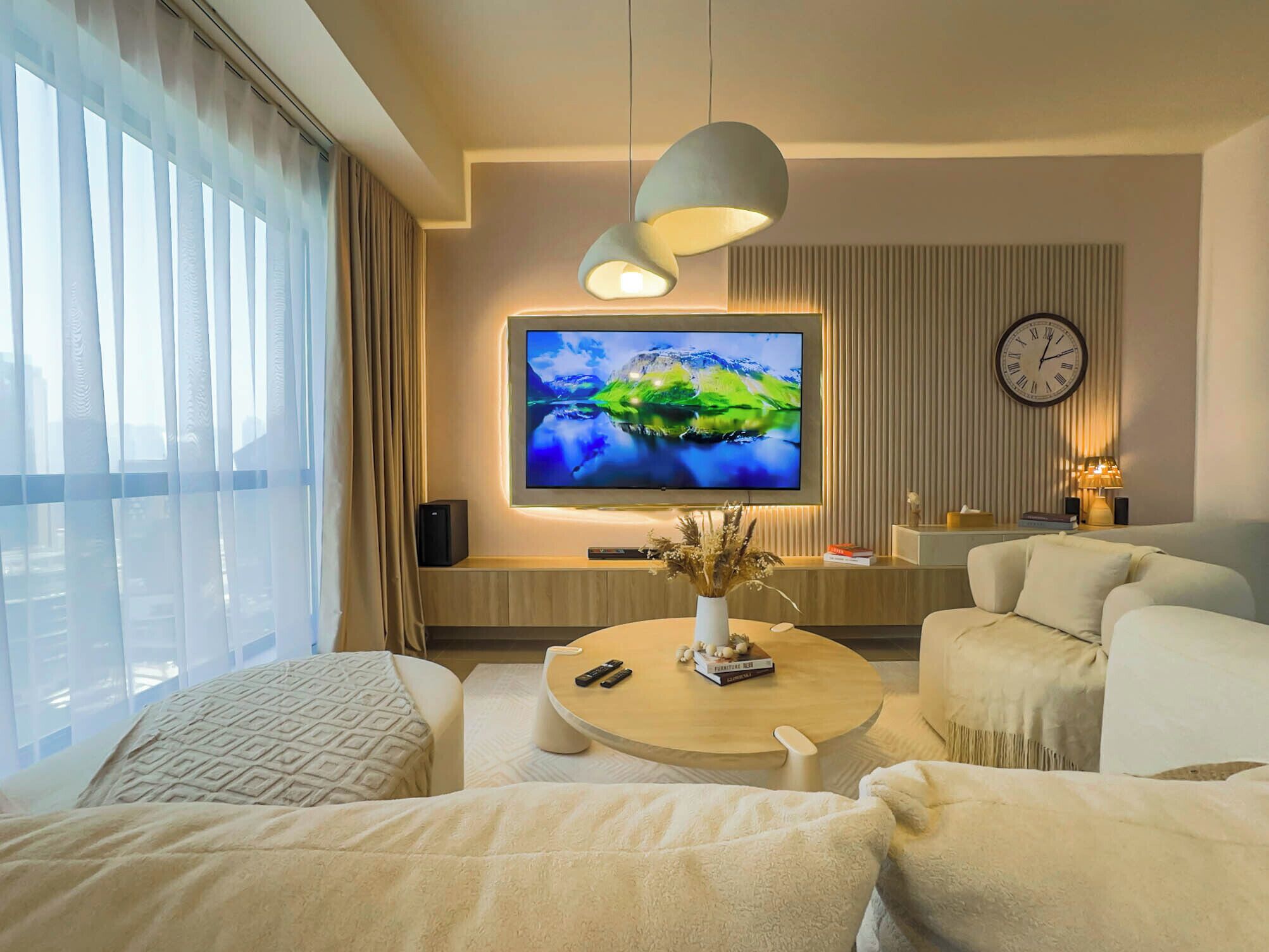 A modern living room with a large flat-screen TV, a round coffee table, and two sofas.