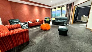 A modern room with a red accent wall, two leather sofas, a black armchair, a green ottoman, and a large window offering a view. - Spacious Escape on Busch Lane (Christchurch)