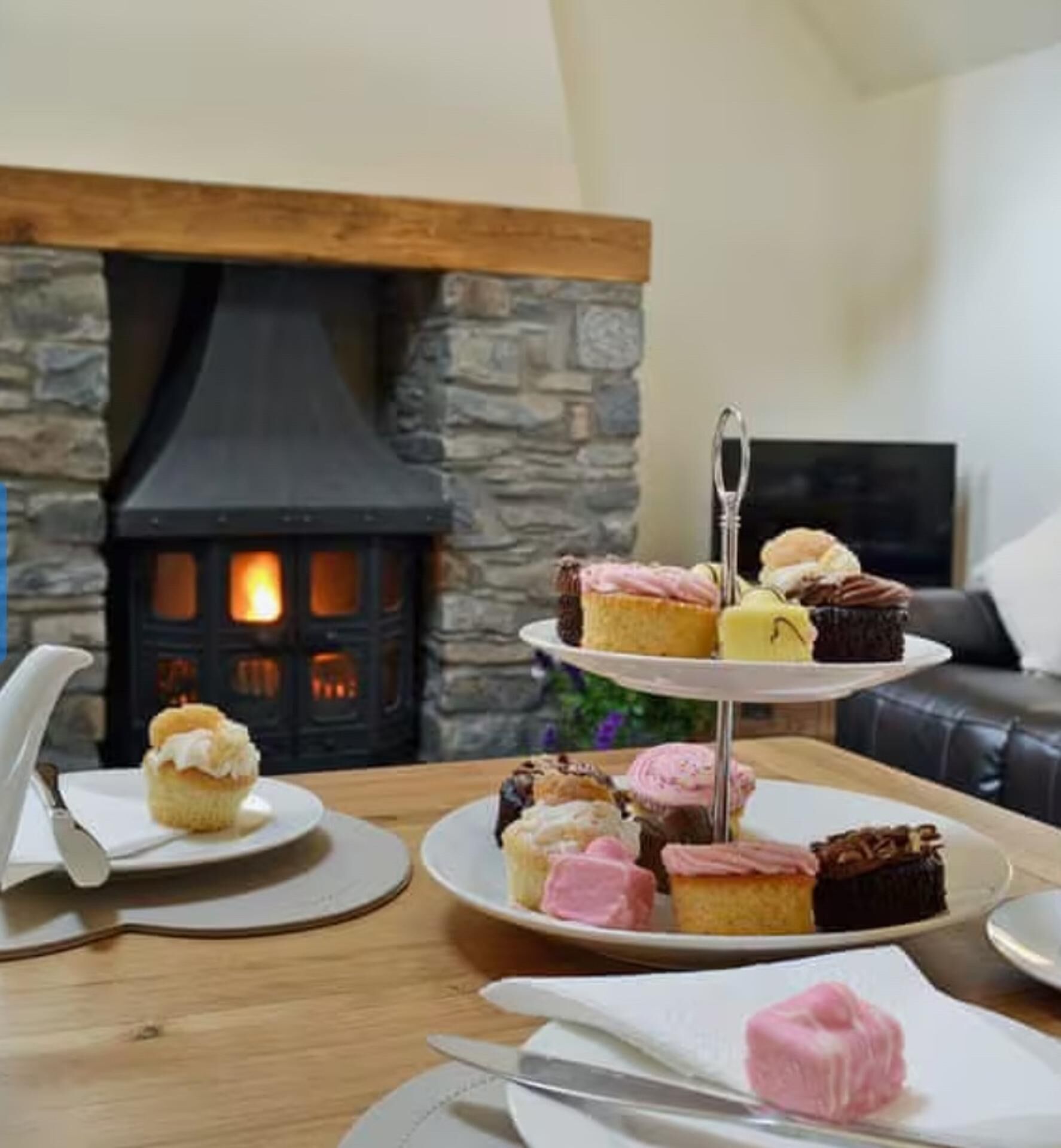 A cozy living room with a stone fireplace, a three-tiered dessert stand, and a leather sofa.