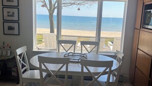 Un comedor con una mesa y sillas, un ventilador de techo y vistas a la playa a través de amplios ventanales.