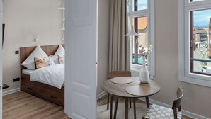 Een slaapkamer met een bed, nachtkastjes, een ronde eettafel met stoelen en een raam met uitzicht op gebouwen.