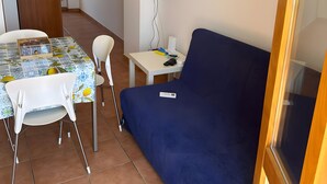 A small room with a sofa, a table with chairs, a television mounted on the wall, and a door leading to another room.