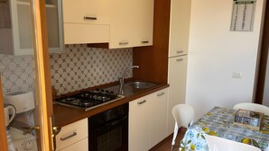 A compact kitchen with white cabinets, a gas stove, a sink, and a dining area with a table and chairs.