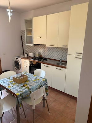 Una cocina compacta equipada con lavadora, cocina a gas y lavamanos. Hay una mesa de comedor con sillas.