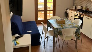 A compact living space with a kitchenette, a dining area with a table and chairs, a sofa, and a television mounted on the wall.