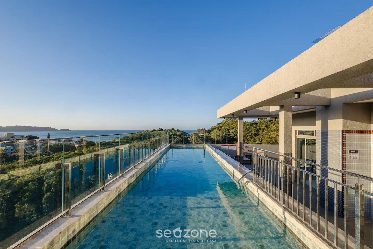 A rooftop infinity pool with a clear view of the sea and distant land.