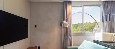 A modern room with a flat-screen TV mounted on the wall, a bed with a patterned bedspread, a bedside table with a decorative item, and a window with curtains.