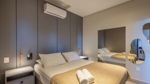 Habitación de hotel moderna con cama, mesitas de noche, unidad de aire acondicionado, espejo montado en la pared y una toalla sobre la cama.