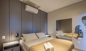 A modern hotel room with a bed, bedside tables, an air conditioning unit, a wall-mounted mirror, and a towel on the bed. - Your Exclusive Stay With Pool and Jacuzzi Just 500 Meters From the Beach - ELF (Bombinhas)