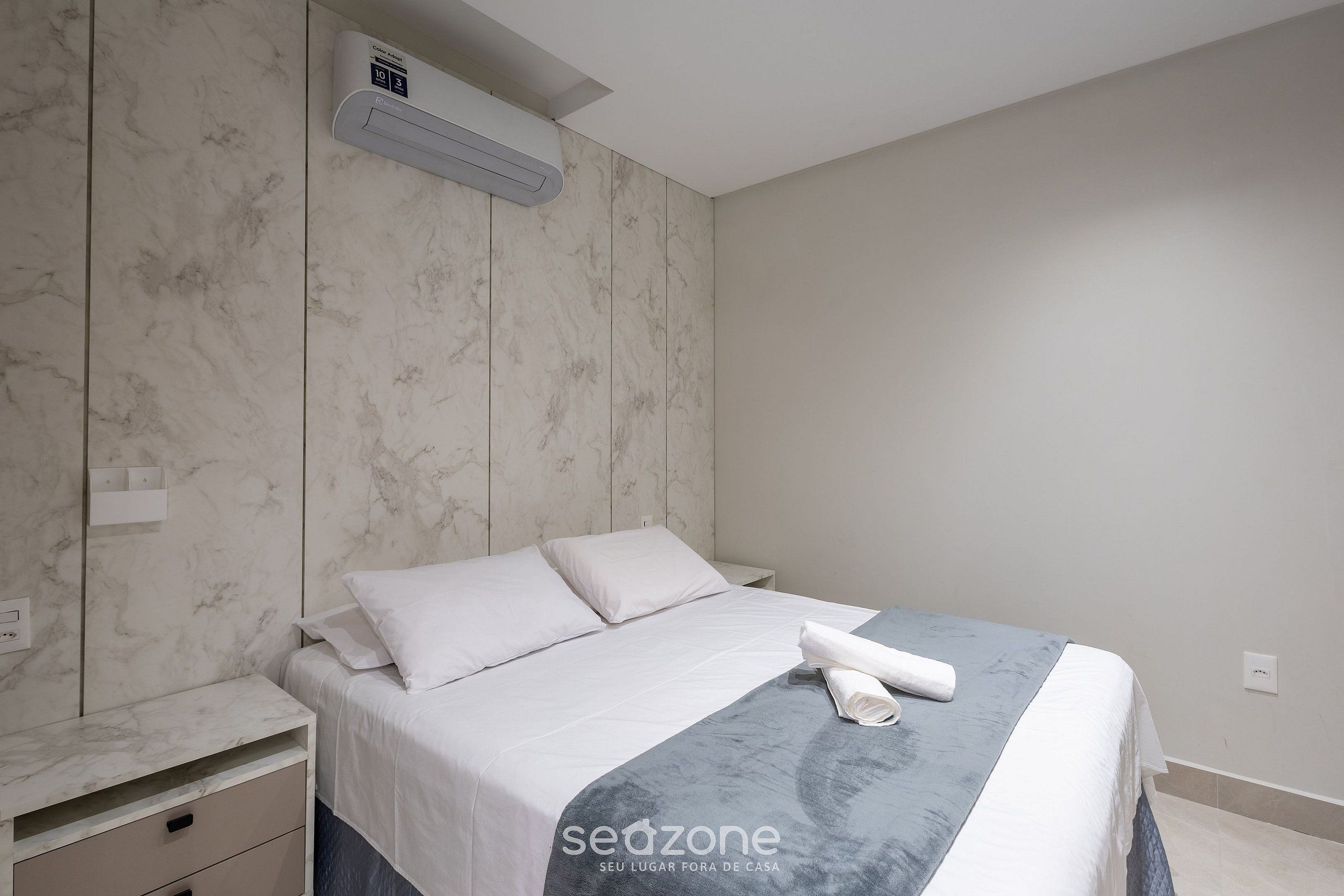 Een moderne slaapkamer met een marmeren muur, een bed met witte lakens en een netjes opgemaakt dekbed.