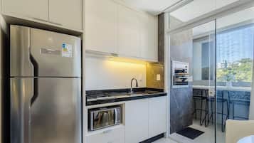 A modern kitchen with a built-in oven, a stainless steel refrigerator, and a glass door leading to a balcony with outdoor seating.