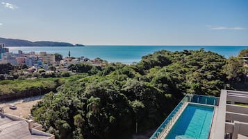 A residential area with a swimming pool, dense greenery, and a view of the sea.