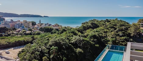 Área residencial com piscina, vegetação densa e vista para o mar.