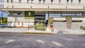 A modern building with a flat facade, a sign for "Capital Empreendimentos," and a gated entrance with a staircase leading up.