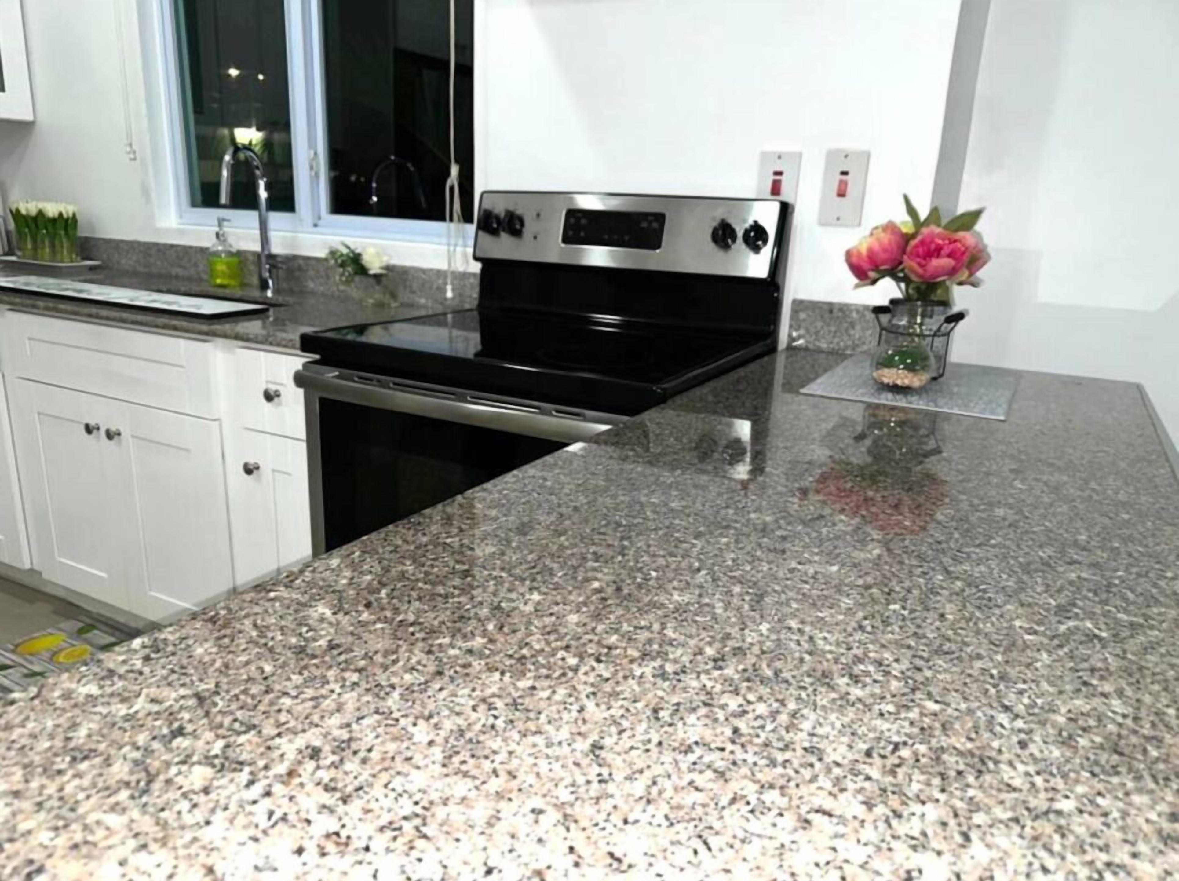 Una cocina con encimeras de granito, horno de acero inoxidable, armarios blancos y un ventanal con vistas.