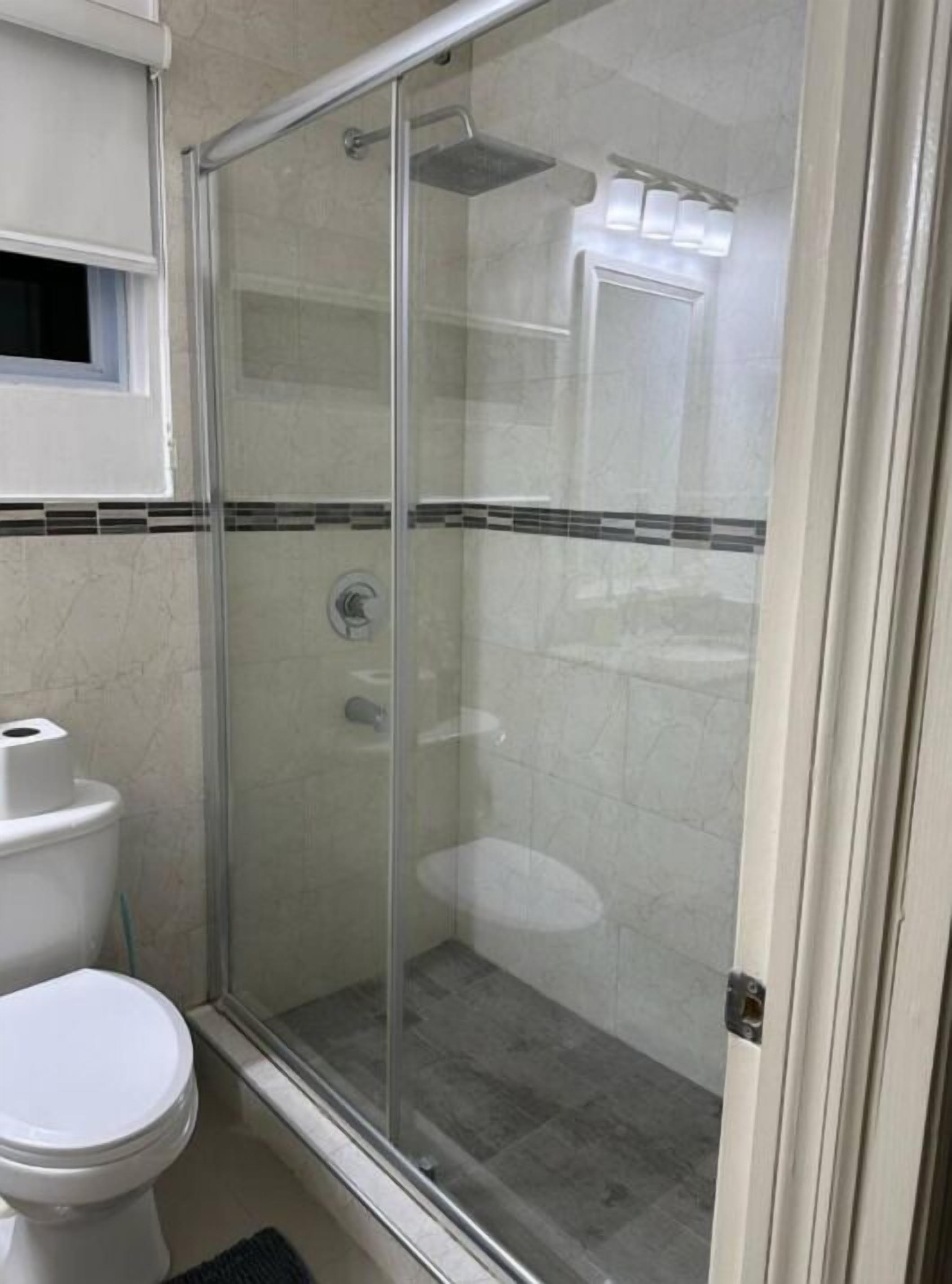 A bathroom with a glass-enclosed shower, a toilet, and a sink.