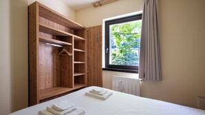 A bedroom with a wooden wardrobe, a radiator, and a window with a view of greenery.